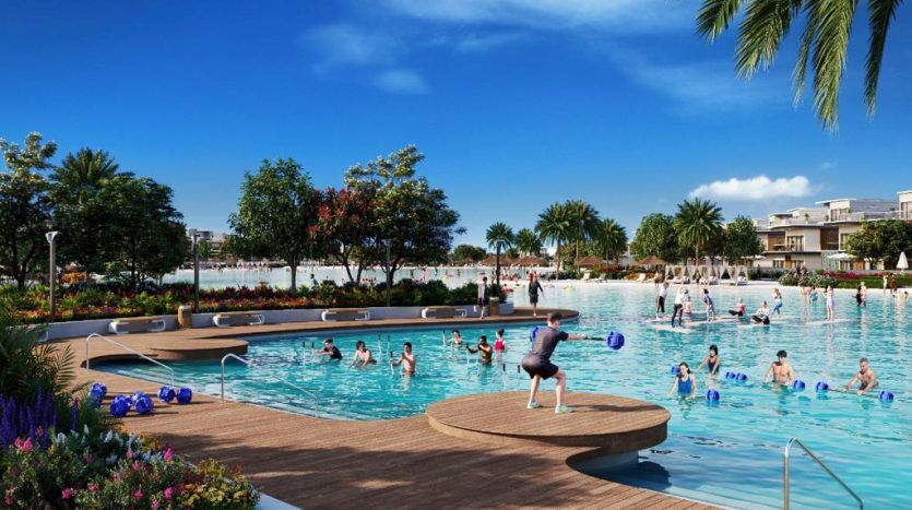 Une piscine extérieure animée dans une villa luxueuse à Dubaï grouillant de monde ; comprend des terrasses en bois élégantes, des structures gonflables dispersées et des rangées de chaises longues sous un ciel ensoleillé.