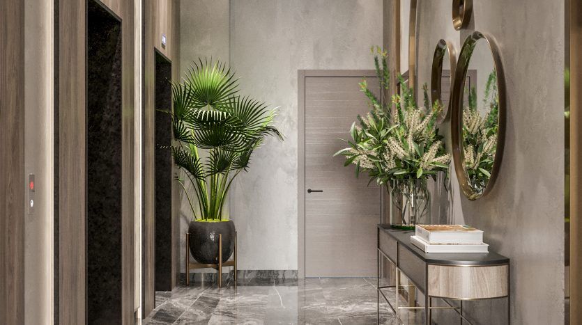 Un hall d'entrée moderne et élégant avec des sols en marbre brillant, des murs gris, des accents dorés et des plantes vertes luxuriantes. Il y a un ascenseur sur la gauche et un coin salon élégant avec des miroirs circulaires sur la droite.