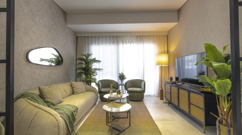 Un salon moderne et confortable dans un appartement de Dubaï avec un canapé beige, deux fauteuils verts, une table basse ronde, une grande télévision, des plantes et un éclairage tamisé provenant de plafonniers cachés et d'un grand