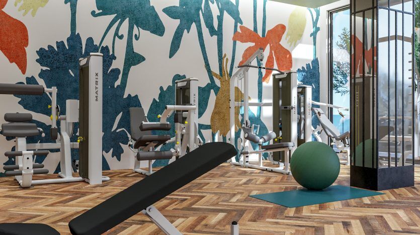 Un intérieur de salle de sport moderne dans une villa de Dubaï comprenant des équipements d'haltérophilie, un ballon d'exercice et des œuvres d'art murales florales colorées. La pièce dispose de grandes fenêtres, de parquet et d'un élégant panneau de miroir.