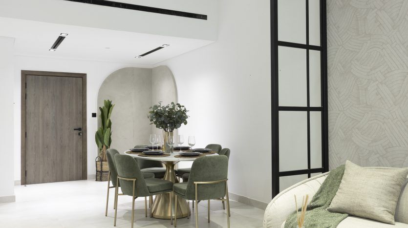 Salle à manger moderne avec table ronde et chaises rembourrées vertes, table élégante, à côté d'un coin salon confortable avec canapé et coussins dans un appartement de Dubaï, aux tons neutres et à la décoration minimaliste