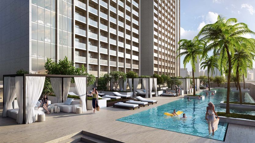 Piscine luxueuse de l'hôtel avec des gens se détendant sur des chaises longues et des cabanes, entourée de grands immeubles et de palmiers, sous un ciel clair à Dubaï.