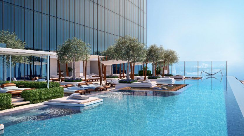 Une luxueuse piscine à débordement offrant une vue panoramique avec des chaises longues, des cabanes et des arbres décoratifs à côté d'un immeuble de grande hauteur à Dubaï.