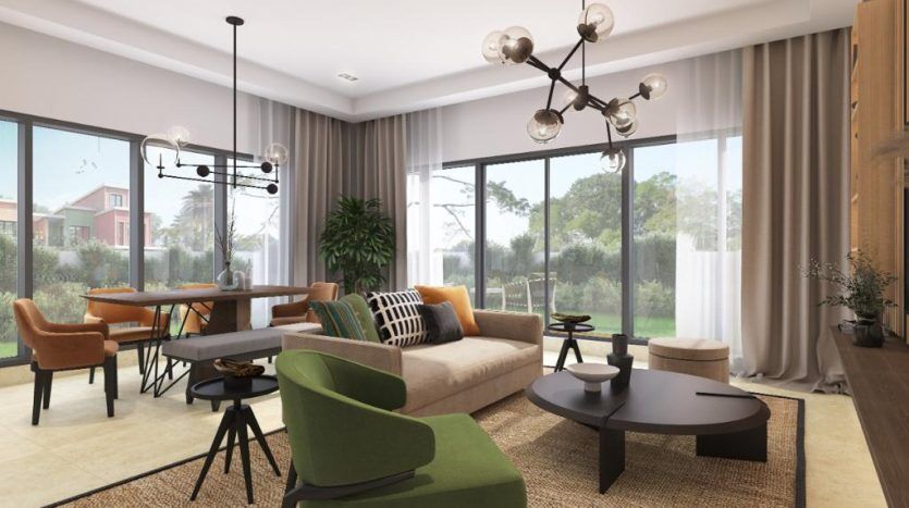 Salon moderne avec de grandes fenêtres donnant sur un jardin dans une villa de Dubaï, comprenant un canapé vert, des tables basses rondes et un coin repas avec des chaises orange. Le décor comprend un lustre et des plantes en pot