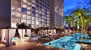 Espace piscine luxueux de l'hôtel au crépuscule, doté d'une piscine éclairée entourée de cabanes privées et de palmiers, avec une façade de villa de Dubaï en arrière-plan.