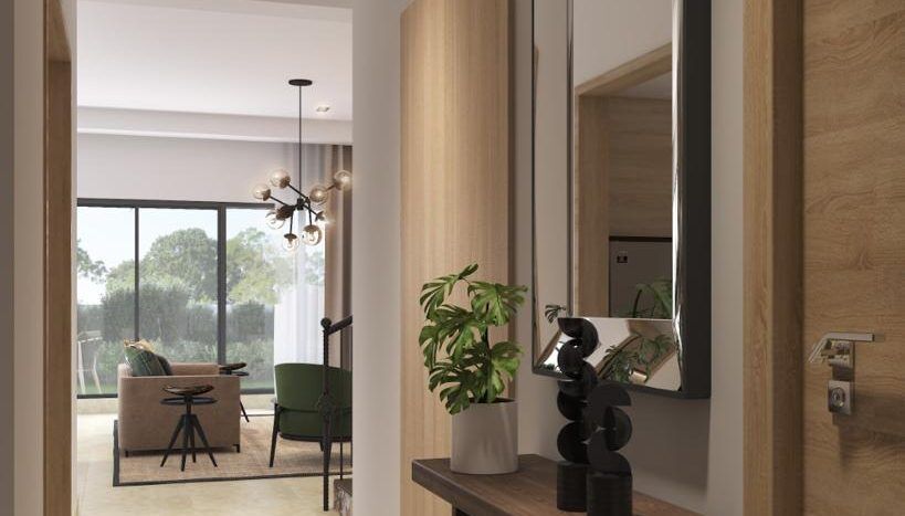 Un intérieur de villa moderne à Dubaï comprenant un couloir avec des murs en bois clair, un miroir rectangulaire, une console sombre avec une sculpture et une plante, menant à un salon lumineux avec des meubles visibles dans le
