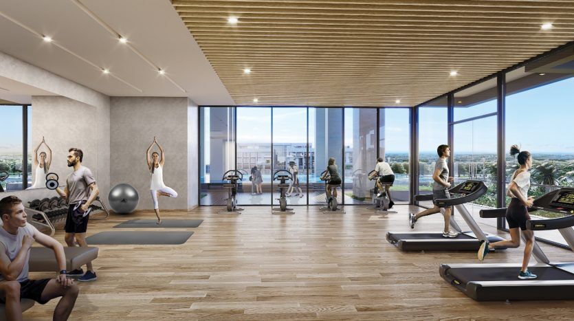 Salle de sport moderne dotée de fenêtres panoramiques, accueillant des personnes pratiquant diverses activités comme le yoga, la course sur tapis roulant et l'haltérophilie. Magnifique horizon de la ville de Dubaï en arrière-plan.