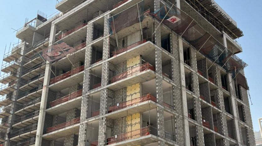 Un bâtiment à plusieurs étages en construction avec des échafaudages et une charpente apparente sur un ciel bleu clair, mettant en évidence le potentiel d'investissement à Dubaï.