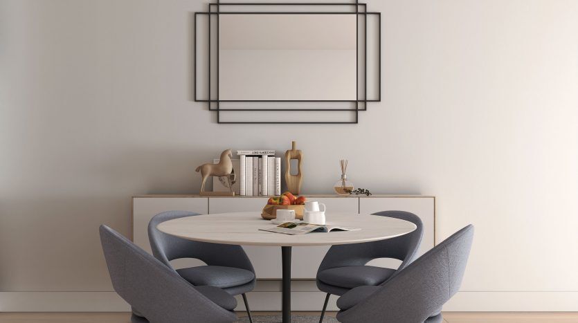 Une salle à manger moderne dans une villa de Dubaï comprenant une table ronde blanche avec quatre chaises grises sur un tapis circulaire bleu, un cadre mural géométrique décoratif au-dessus et une configuration simple pour le petit-déjeuner.