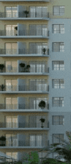 Image verticale d'une partie d'un immeuble d'appartements moderne à Dubaï avec des balcons, chacun décoré de plantes vertes. Quelques personnes sont visibles sur les balcons profitant de l'espace extérieur.