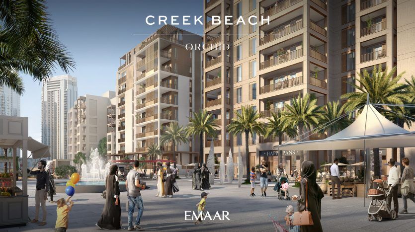 Cette image représente une place urbaine moderne et animée entre de grands immeubles de villas résidentielles à Dubaï, remplie de piétons, de cyclistes et de vendeurs, sous un ciel dégagé. Des panneaux identifient la zone comme étant « Creek Beach