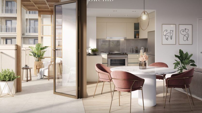 Intérieur d'appartement moderne à Dubaï comprenant un coin repas avec une table ronde en marbre et des chaises roses, relié à une cuisine élégante et un balcon extérieur, baigné de lumière naturelle.