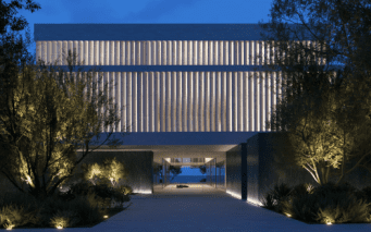 Bâtiment moderne de Dubaï éclairé au crépuscule avec un design symétrique comportant une passerelle centrale menant sous une grande structure surélevée flanquée de rangées d'arbres.