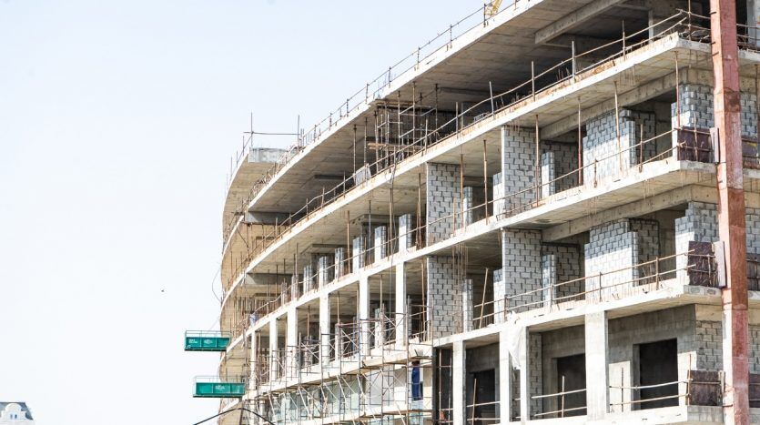 Une villa en béton à plusieurs étages en construction à Dubaï avec des échafaudages visibles et des panneaux sur le bâtiment indiquant « développeurs sûrs » et « gardénia ».