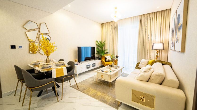 Un salon moderne avec un coin repas au décor élégant, un canapé moelleux, un miroir mural géométrique et une table à manger pour quatre, le tout sous un éclairage ambiant doux dans une villa haut de gamme de Dubaï.