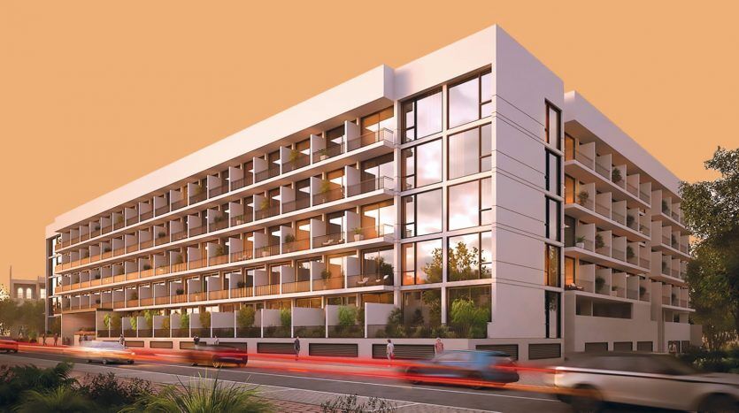Extérieur d'un immeuble d'appartements moderne à Dubaï au coucher du soleil avec des fenêtres éclairées et une circulation floue au premier plan.