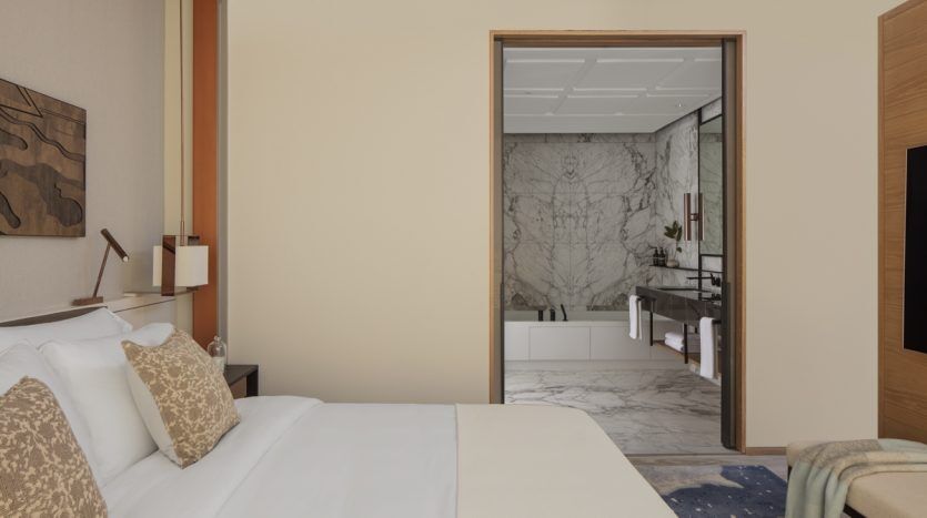 Une chambre moderne dotée d'un lit moelleux avec des oreillers décoratifs et une vue sur une luxueuse salle de bains en marbre attenante. Les tons chauds et neutres et la décoration contemporaine d'un appartement Dubaï renforcent l'atmosphère élégante.