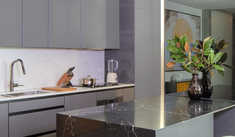 Cuisine moderne comprenant un îlot en marbre avec un comptoir en marbre noir, des armoires grises et des appareils électroménagers en acier inoxydable. Un vase aux feuilles vertes ajoute une touche de fraîcheur. La lumière naturelle illumine l'espace dans ce magnifique