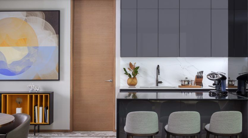 Intérieur de cuisine moderne avec comptoir en marbre, armoires grises et porte coulissante en bois dans un appartement Dubaï. Comprend un tableau, des tabourets et des plantes décoratives.
