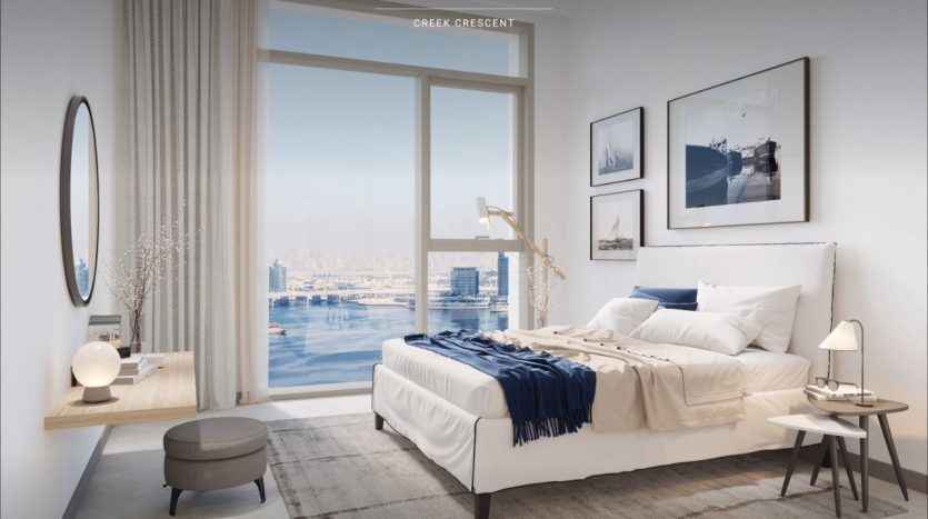 Chambre moderne dans un appartement de Dubaï surplombant la crique de Dubaï avec un grand lit, des touches bleues et une décoration minimaliste. Une baie vitrée offre une vue sur les toits de la ville.