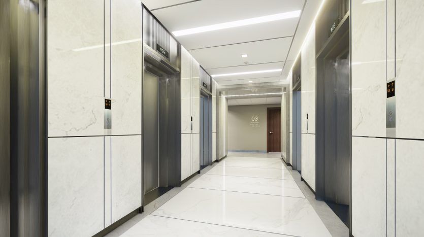 Un hall d'ascenseur moderne avec des sols et des murs en marbre, comprenant deux ascenseurs avec indicateurs d'étage numériques et un couloir menant à une porte marquée « 03 » dans un immeuble prestigieux de l'immobilier de Dubaï.
