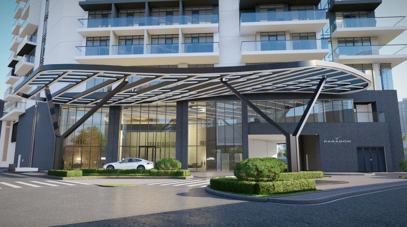 Entrée d'un immeuble d'appartements moderne à Dubaï avec un élégant auvent métallique incurvé, une verdure paysagée de chaque côté et une voiture blanche garée devant. Le bâtiment dispose de grandes portes et fenêtres vitrées.