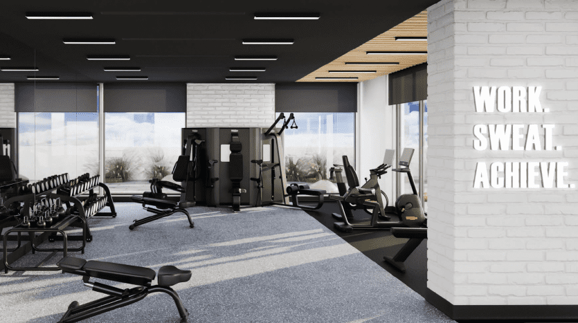 Intérieur de salle de sport moderne avec équipement d'exercice comprenant des tapis roulants et des bancs de musculation, avec un texte mural de motivation « investissement Dubaï ». et de grandes fenêtres donnant sur un paysage serein.