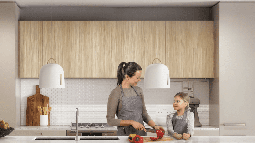 Une mère et sa fille préparent à manger ensemble dans une villa moderne de Dubaï dotée d'armoires en bois. La mère coupe des légumes tandis que la fille regarde avec impatience.