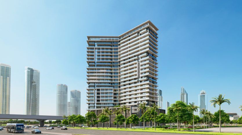 Un immeuble résidentiel moderne de grande hauteur avec de grands balcons, situé dans une zone urbaine avec un aménagement paysager verdoyant et plusieurs autres gratte-ciel sous un ciel bleu clair, parfait pour ceux qui s'intéressent à l'immobilier Dubaï.