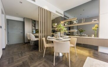 Cuisine et salle à manger modernes dans un appartement de Dubaï avec un mobilier élégant, une table à manger en bois pour deux personnes, des comptoirs de cuisine élégants et des fleurs décoratives, avec un parquet à chevrons et une palette de couleurs neutres