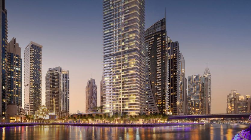 Gratte-ciels le long d'un front de mer à Dubaï illuminés au crépuscule, avec des reflets dans l'eau et une passerelle qui les traverse.