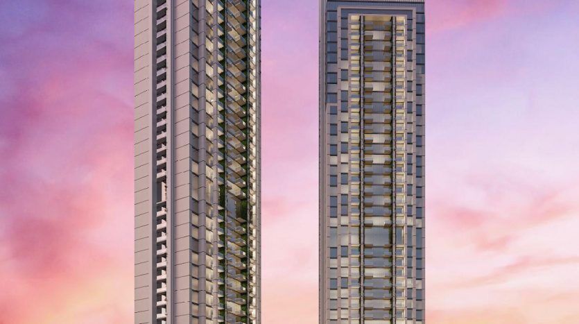 Deux immeubles d'appartements modernes de grande hauteur sur un ciel de coucher de soleil rose et orange vif, avec un horizon lointain de Dubaï en arrière-plan.