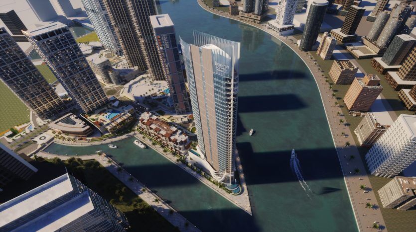 Vue aérienne d'un paysage urbain moderne présentant un bâtiment imposant, haut et incurvé sur un front de mer à Dubaï, entouré de nombreux autres immeubles de grande hauteur, d'espaces verts et de bateaux sur l'eau.