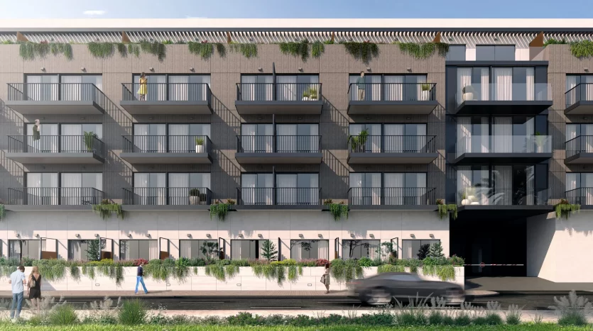 Façade d'immeuble d'appartements moderne à Dubaï avec balcons ornés de plantes vertes, voiture floue passant et piétons marchant devant. Il y a un ciel clair au-dessus et des notes de végétation sur les côtés.