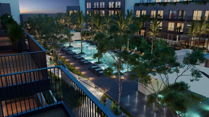 Vue nocturne d'un luxueux balcon d'hôtel donnant sur une piscine éclairée entourée de palmiers, avec des façades de bâtiments modernes en arrière-plan à Dubaï.
