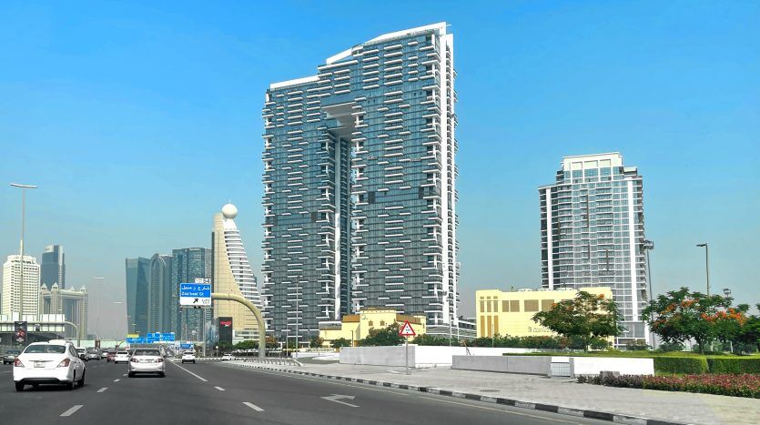 Une rue animée de Dubaï avec des gratte-ciel modernes sous un ciel bleu clair. Les voitures roulent sur la route et un gratte-ciel unique et sinueux domine l'horizon.