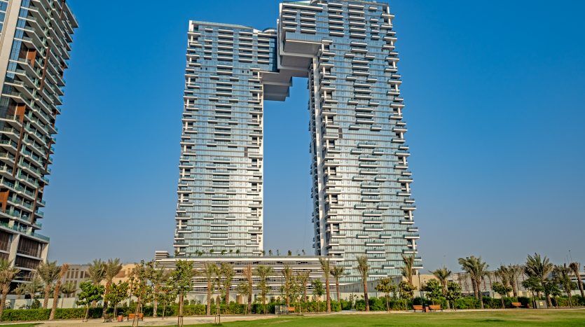 Immeuble d'appartements architectural moderne à Dubaï avec un design unique en forme de U, entouré de parcs verdoyants et d'un ciel bleu clair.