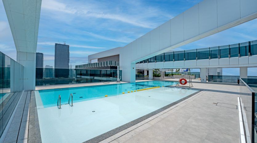 Une piscine moderne sur le toit entourée de barrières de verre et de bâtiments blancs élégants sous un ciel bleu clair, avec des gratte-ciel visibles en arrière-plan. Ce cadre haut de gamme est une opportunité d'investissement idéale à Dubaï