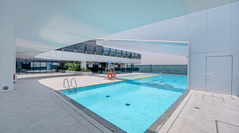 Une piscine extérieure sur un toit au design moderne et minimaliste avec des lignes épurées et une eau bleu clair. La zone, qui fait partie d'un projet d'investissement Dubaï, est entourée de barrières de verre et possède une