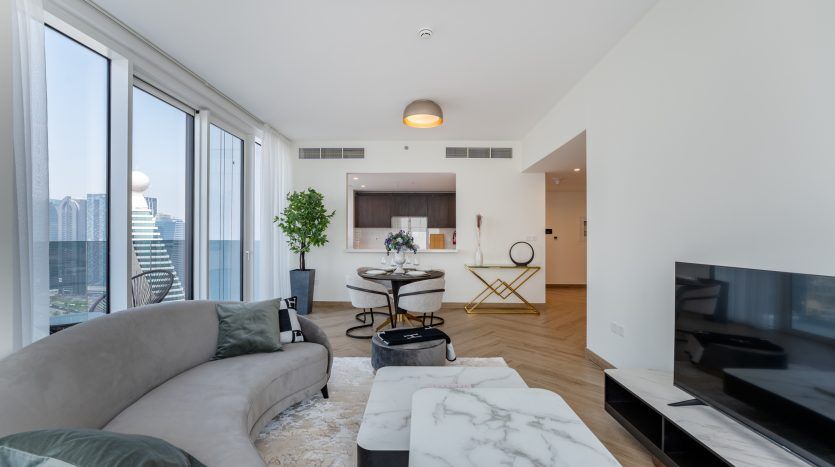 Salon moderne dans un appartement de grande hauteur à Dubaï comprenant un canapé sectionnel, une table basse en marbre, un coin repas et de grandes fenêtres avec vue sur la ville.