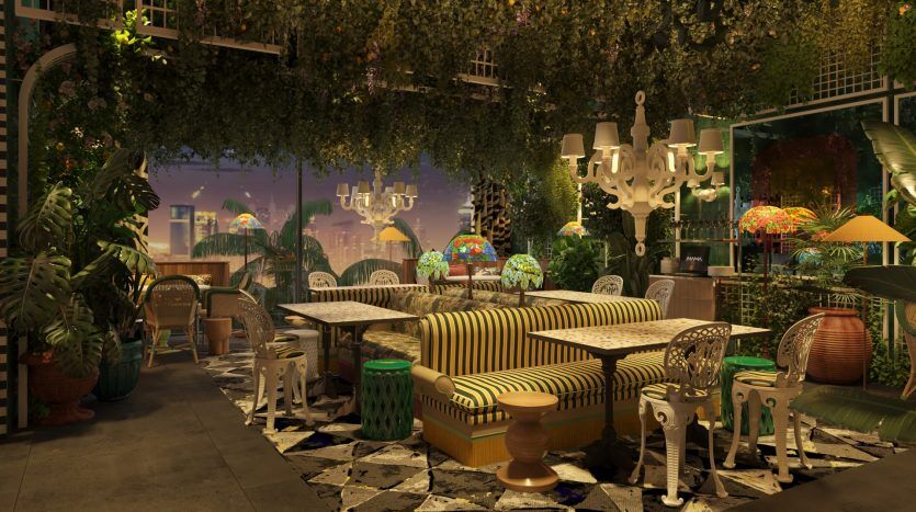 Une salle à manger extérieure éclectique le soir, dotée de canapés à motifs, de lampes suspendues colorées et d'une verdure luxuriante, avec un paysage urbain de Dubaï visible en arrière-plan.