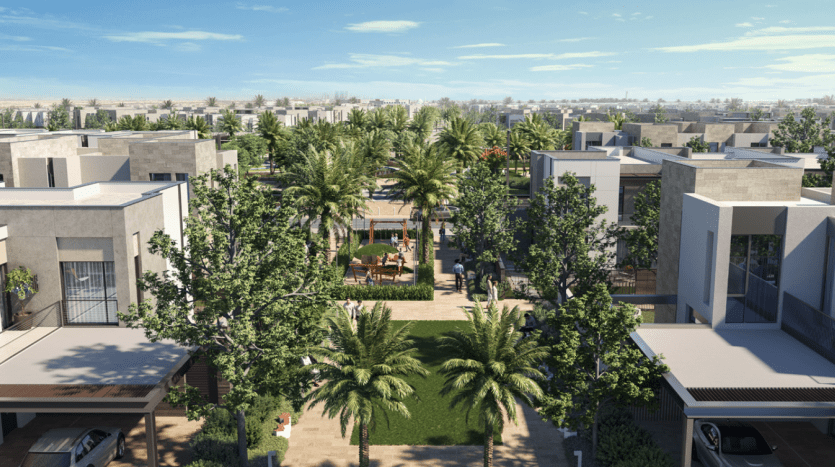 Vue aérienne d'une communauté résidentielle moderne avec des appartements à toit plat, une verdure luxuriante, des palmiers et un espace commun central avec tables et chaises sous parasols. Plusieurs voitures sont garées