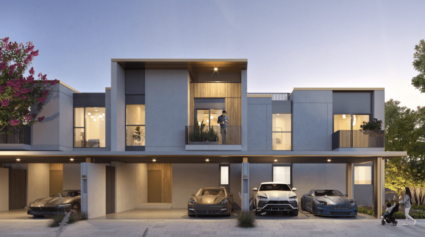 Complexe d'appartements moderne de deux étages à Dubaï au crépuscule avec des intérieurs bien éclairés, avec des balcons, des voitures garées dans des abris d'auto et un couple debout sur un balcon. Des arbres et un piéton sont également visibles