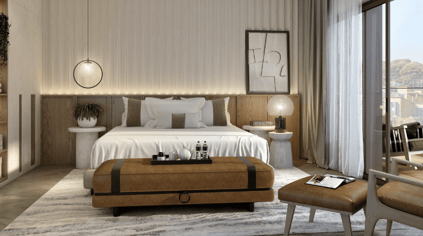 Chambre moderne dotée d'un lit soigneusement fait avec des draps blancs, flanqué de tables de nuit en bois et de lampes élégantes. Un banc moelleux se trouve au pied du lit. La grande fenêtre offre une vue sur le vert