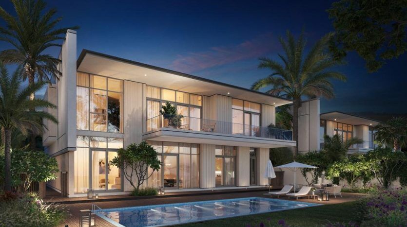 Une luxueuse maison à deux étages éclairée au crépuscule, avec de grandes fenêtres et balcons, entourée de palmiers. Au premier plan, une piscine accueillante avec une chaise longue met en valeur cette propriété de premier ordre de l'immobilier Dubaï.