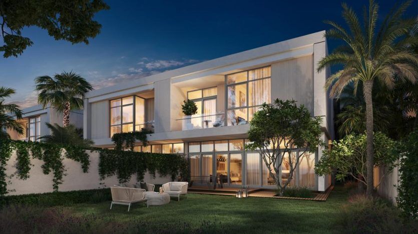 Maison moderne de deux étages à Dubaï éclairée au crépuscule avec de grandes fenêtres, un balcon et entourée de palmiers luxuriants et d'un jardin bien entretenu. Des sièges extérieurs sont visibles sur le patio.