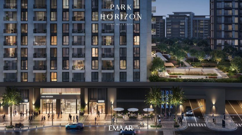 Vue nocturne du bâtiment Park Horizon avec fenêtres éclairées, magasins au rez-de-chaussée et passants. La scène de rue comprend des voitures et des arbres, avec le logo « Emaar » affiché bien en évidence dans cette