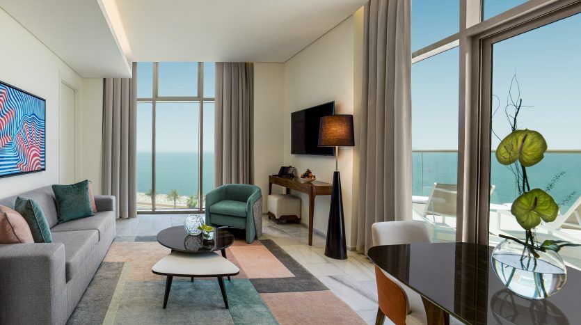Salon moderne à la décoration élégante dans une villa de Dubaï, comprenant un canapé gris, une table basse en verre et de grandes fenêtres offrant une vue panoramique sur l'océan.