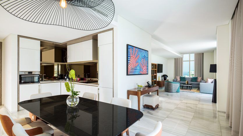 Salon moderne et spacieux dans une villa de Dubaï avec une grande table à manger noire, des chaises élégantes et un plafonnier unique. Il y a une cuisine ouverte, un coin salon confortable et une télévision murale.