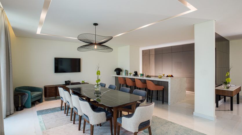 Espace de vie moderne et décloisonné dans une villa de Dubaï comprenant une table à manger avec des chaises, une cuisine avec îlot et un coin salon avec télévision, le tout sous un éclairage contemporain.